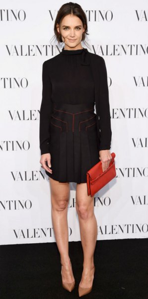 Black mini dress with a high neck, long sleeves, a gathered waist and a clutch bag