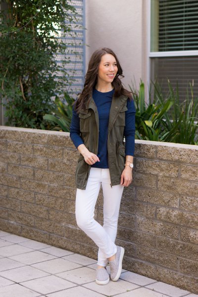 brown utility vest with dark blue long sleeve shirt and white jeans