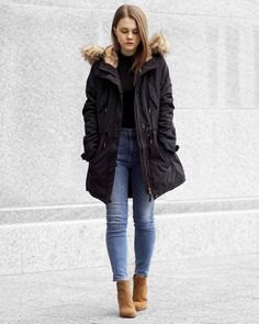 Black long bomber jacket with faux fur hood and slim fitting ankle blue jeans