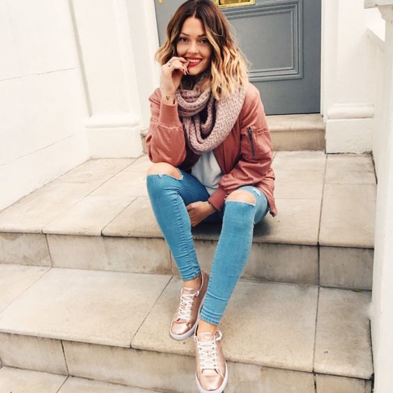 Rouge pink bomber jacket with light blue ripped skinny jeans and gold sneakers
