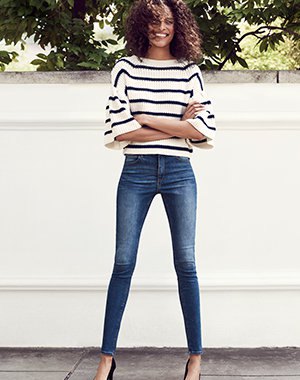 White and black striped sweater with wide sleeves and blue, low-slung drainpipe jeans