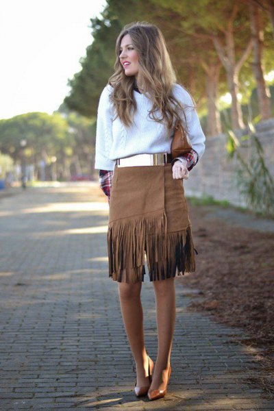 White cable-knit sweater with a metal belt and a knee-length fringed skirt