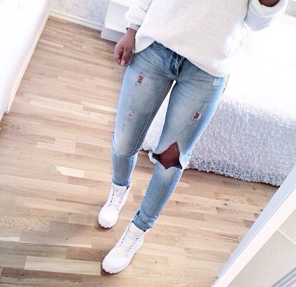 White loose fitting knit sweater with light blue ripped jeans and boots